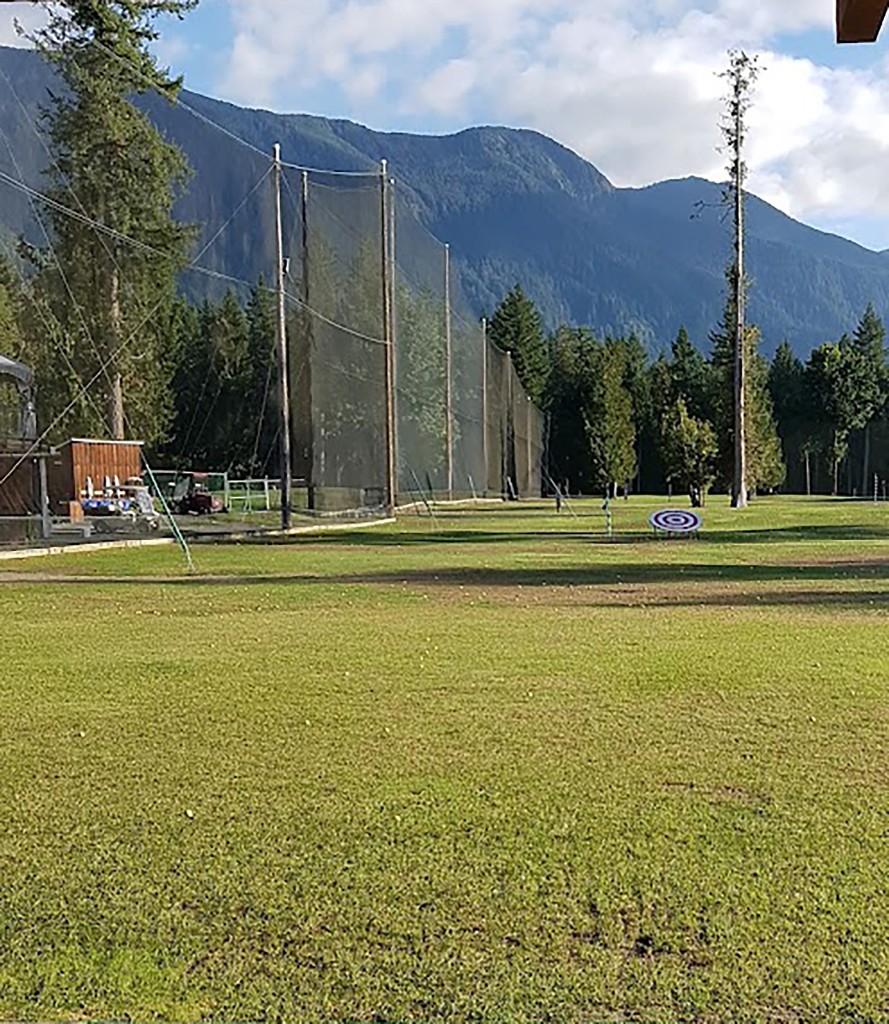 Completed driving range with installed safety netting, practice targets, and mountain backdrop.